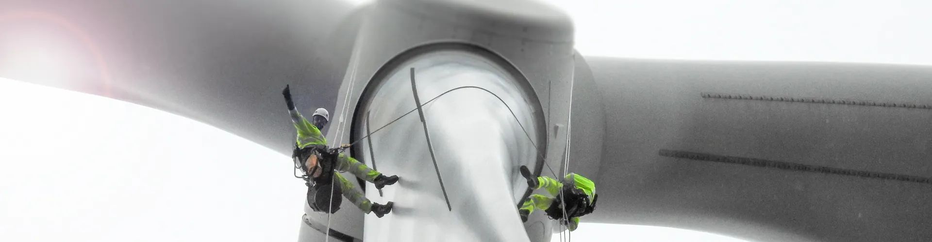 Two rope access technicians doing wind turbine blade inspection and waving