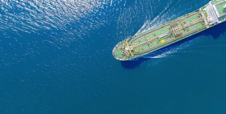 Aerial view of a large ship navigating through deep blue water, with sunlight reflecting off the surface.