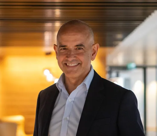 A smiling man in a suit stands in an office hallway.