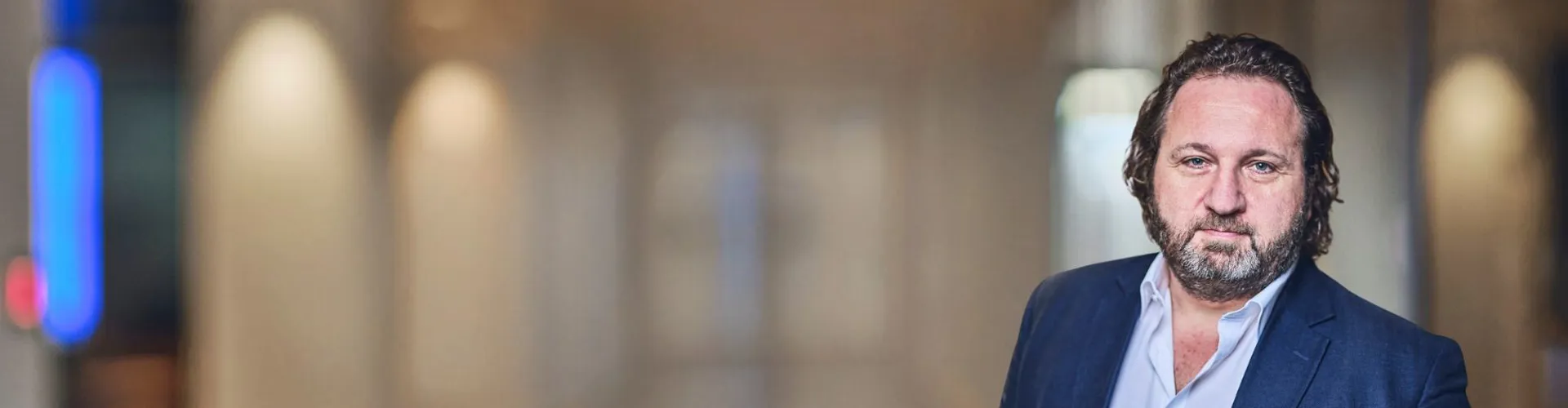 Man in a suit, standing in a blurred hallway.