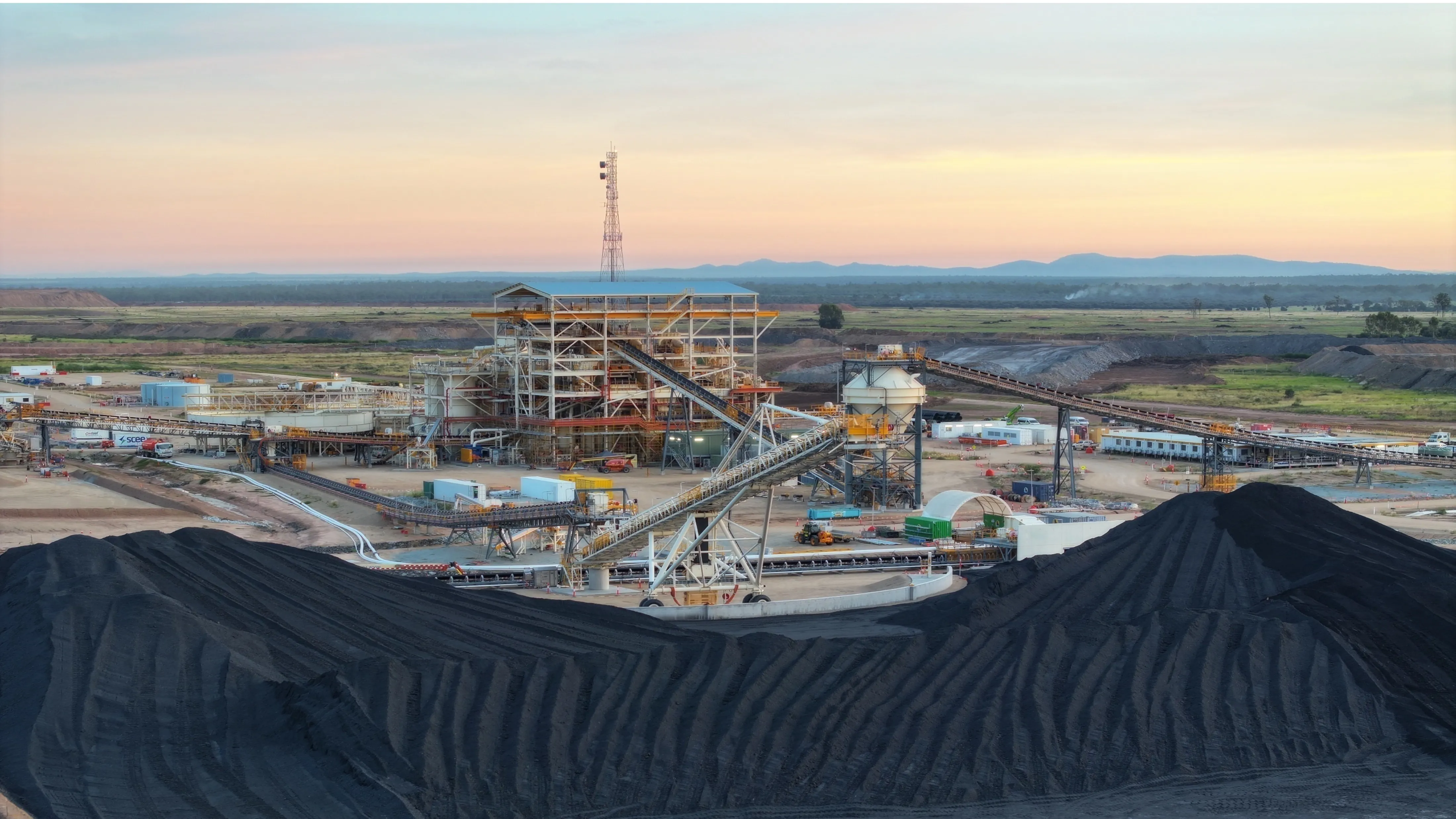 Coal processing facility with coal piles, conveyor belts, and machinery at sunrise.