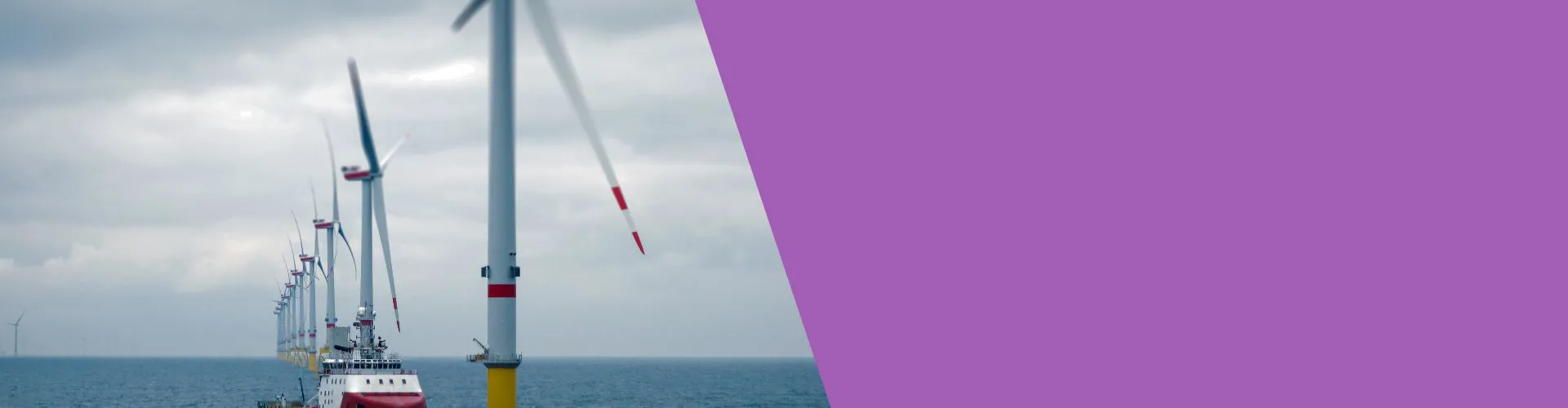 Row of wind turbines over the ocean, cloudy sky.