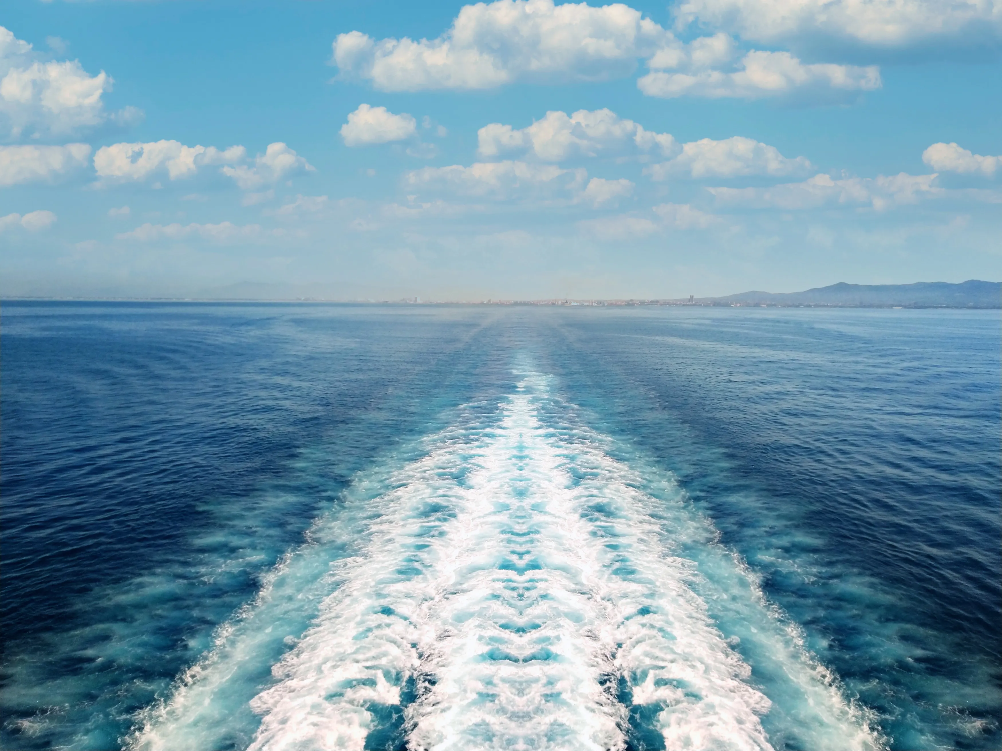 Blue ocean with white wake and scattered clouds.