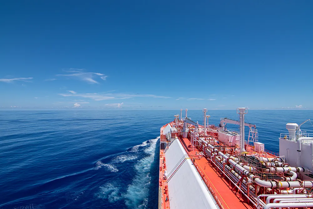 Large cargo ship sailing on calm blue water under a clear sky, leaving a gentle wake.