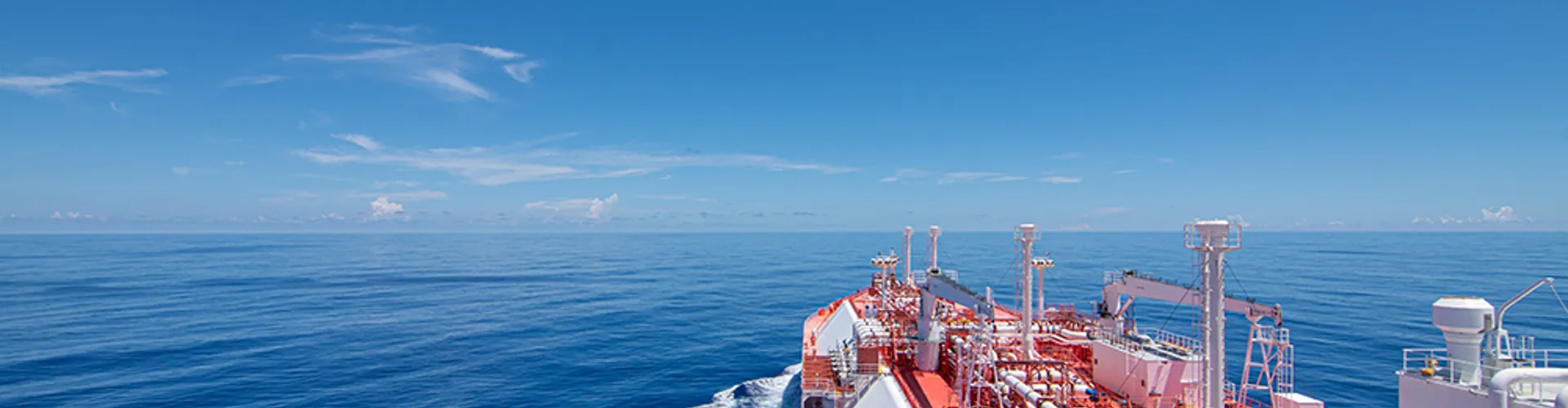 Large cargo ship sailing on calm blue water under a clear sky, leaving a gentle wake.