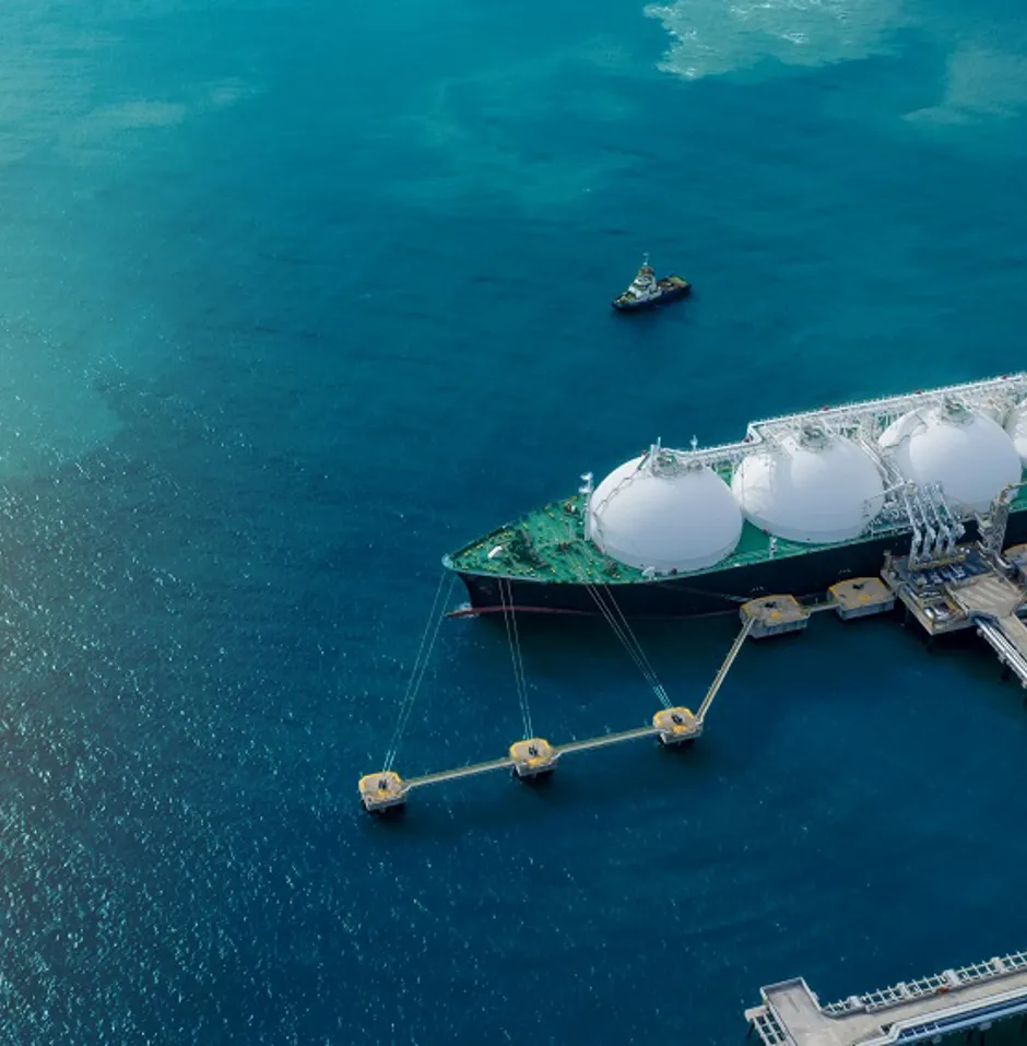 Aerial view of a large ship with three spherical tanks anchored near a dock with pipelines.