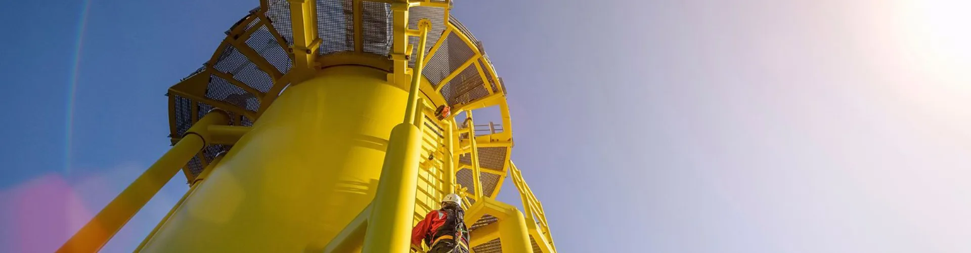 Person in safety gear climbing a bright yellow offshore wind turbine platform.